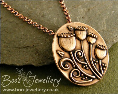 Oval pink bronze pendant featuring seed pods and scrolls