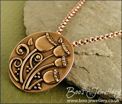 Oval pink bronze pendant featuring seed pods and scrolls