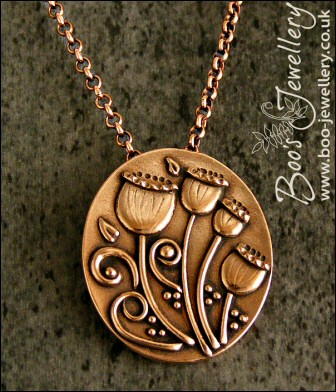 Oval pink bronze pendant featuring seed pods and scrolls