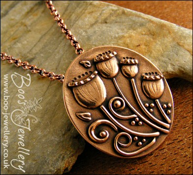 Oval pink bronze pendant featuring seed pods and scrolls