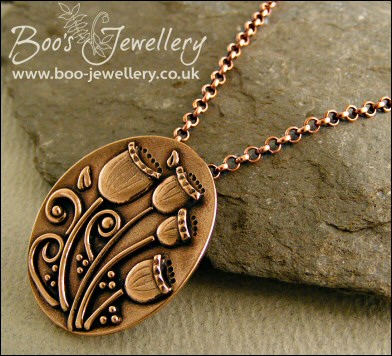 Oval pink bronze pendant featuring seed pods and scrolls