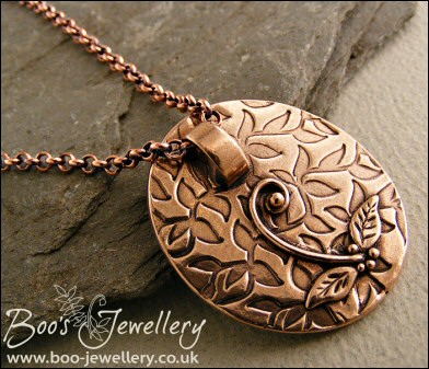 Oval pink bronze pendant featuring seed pods and scrolls